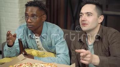 两个朋友在电视上看<strong>体育比赛</strong>。 男人在家里坐在沙发上喝啤酒，吃披萨和零食。